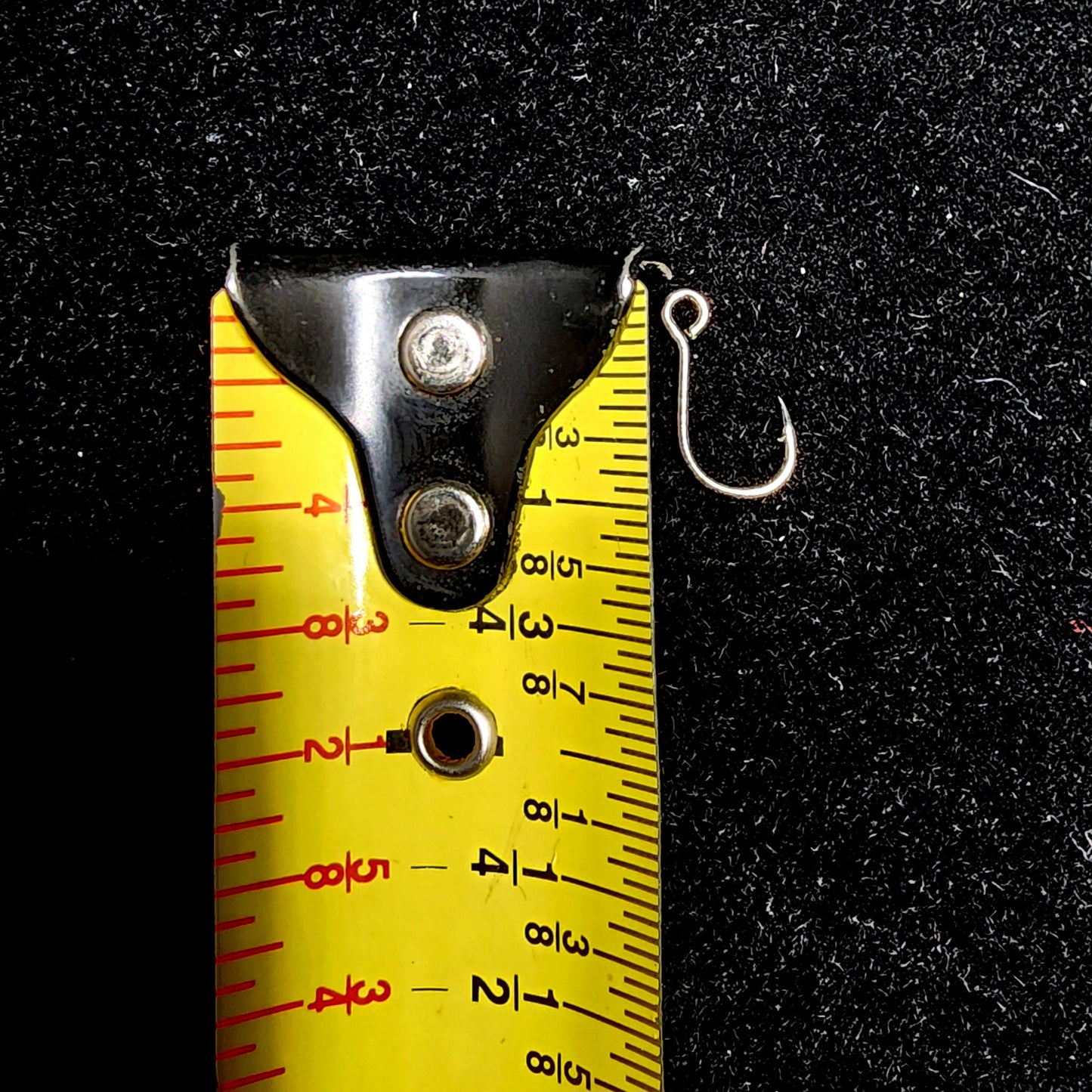Fishing hook next to a yellow measuring tape on a black background
