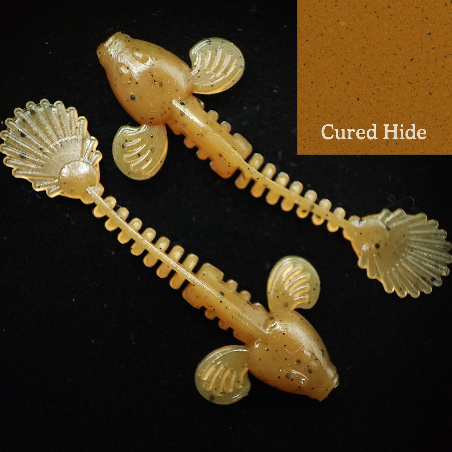 Two beige fishing lures with shell-like ends on a black background, labeled 'Cured Hide'.