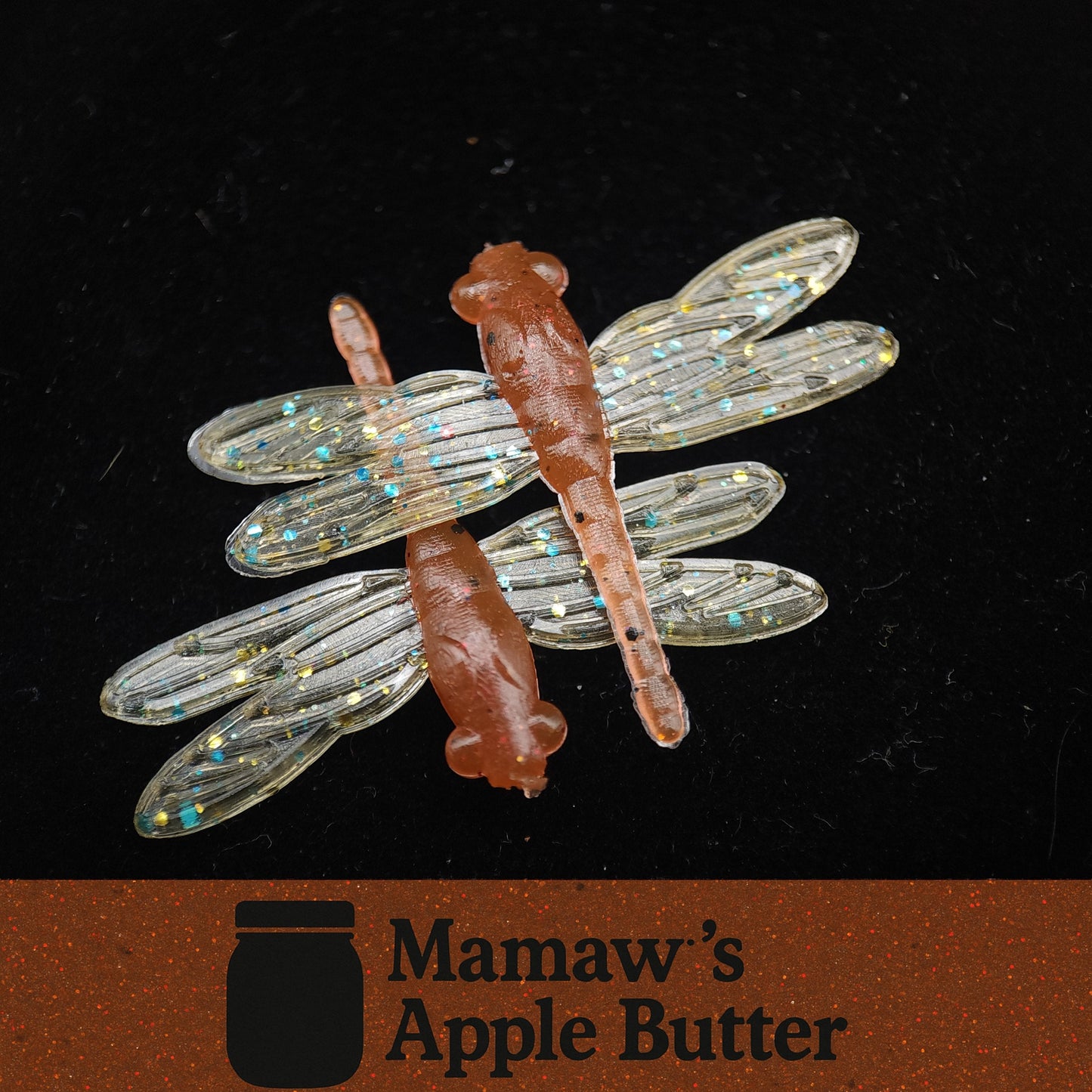 Dragonfly-shaped fishing Lures with clear wings and brown body on a black background, featuring Mamaw's Apple Butter logo.