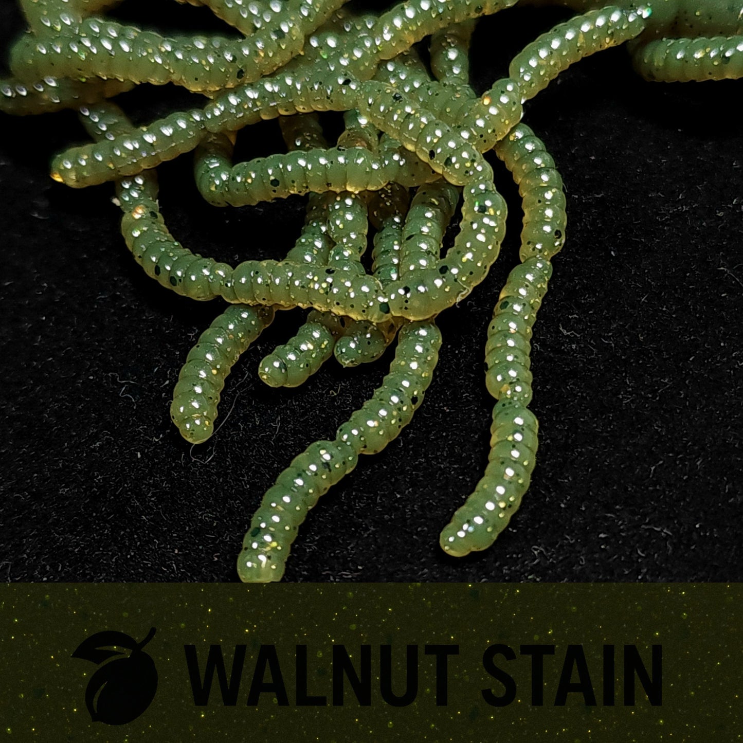Close-up of green larvae fishing lures on a black background with 'Walnut Stain' branding.