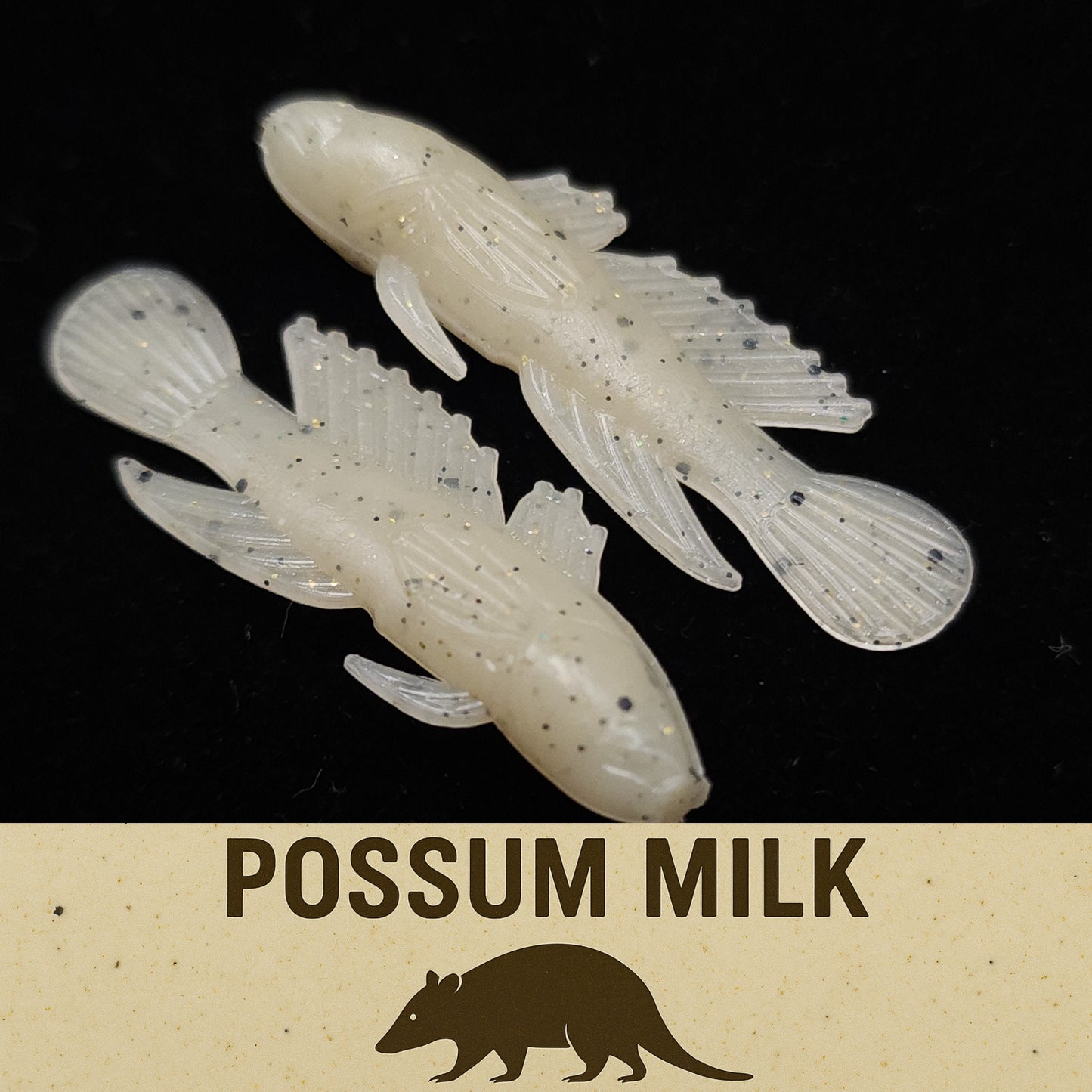 Two white fishing lures with speckles on a black background, labeled 'Possum Milk'.