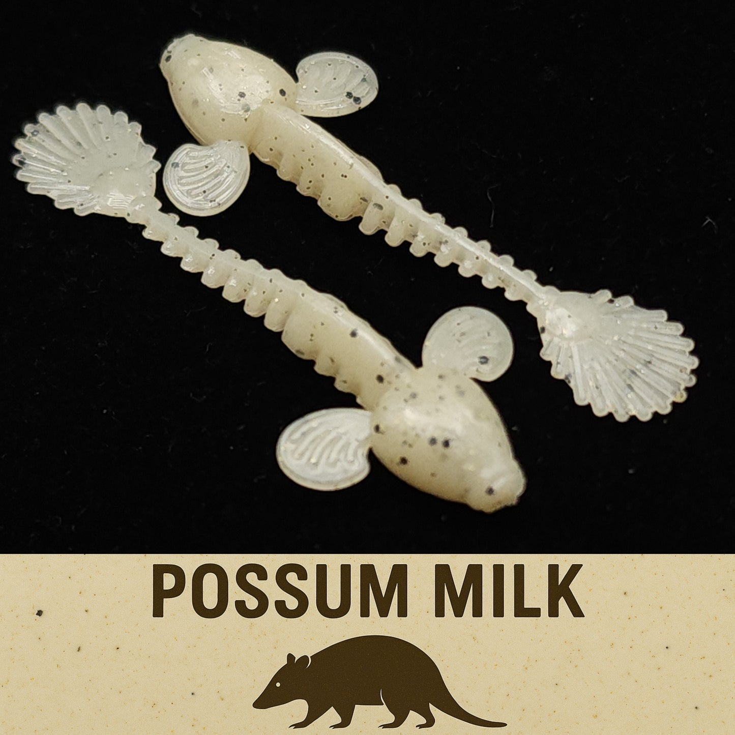Two white fishing lures with shell-like features on a black background, labeled 'Possum Milk'.