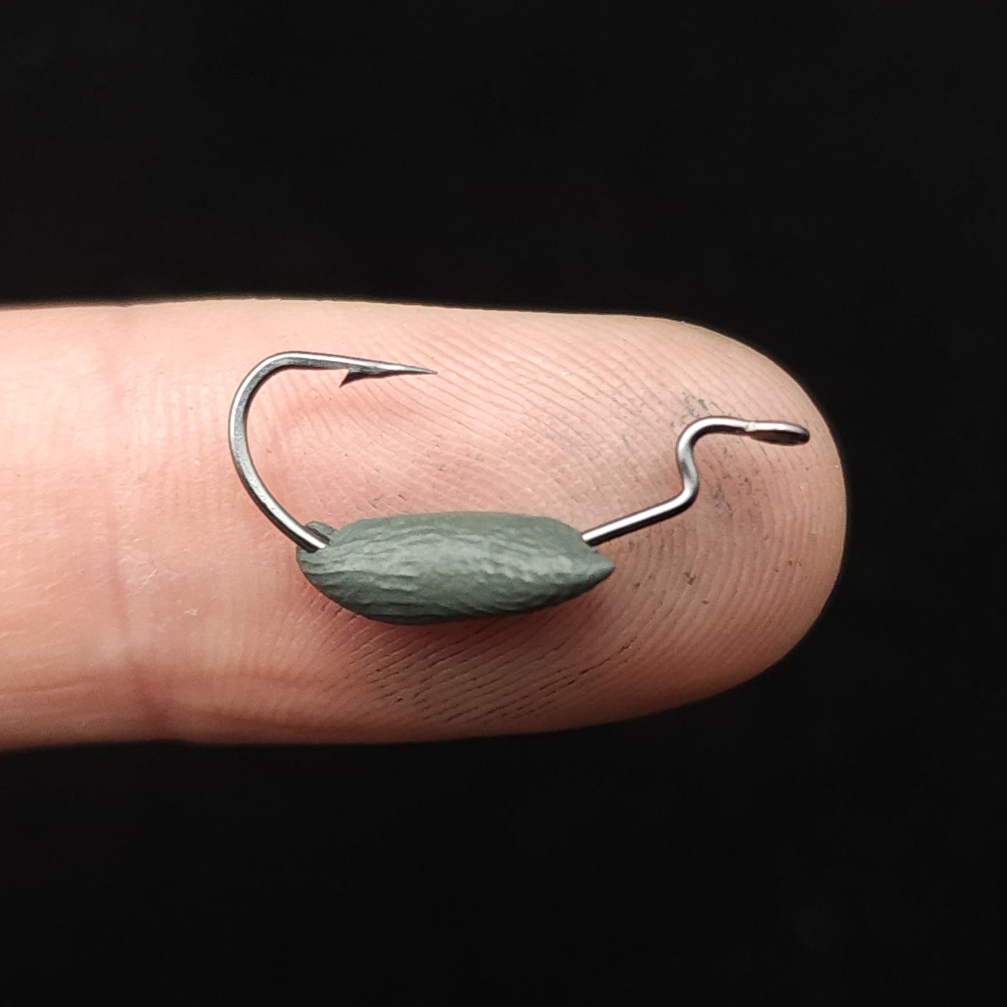 Fishing hook with Creek Life Tungsten Putty on a finger against a black background
