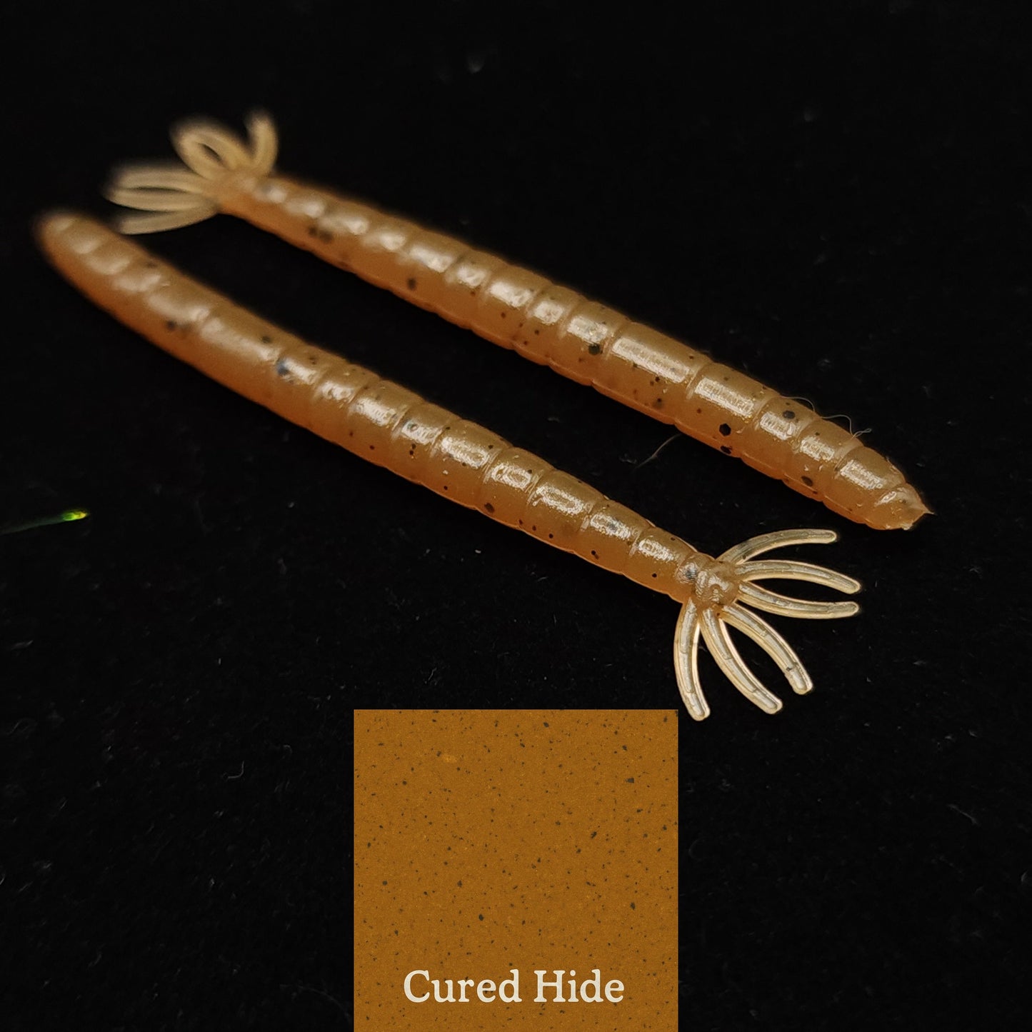 Two centipede  fishing lures on a black background with a color swatch labeled 'Cured Hide'.