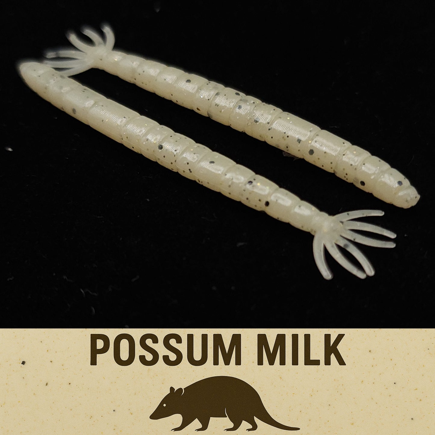 Two white fishing lures with black specks on a dark background, labeled 'Possum Milk' with a possum illustration.