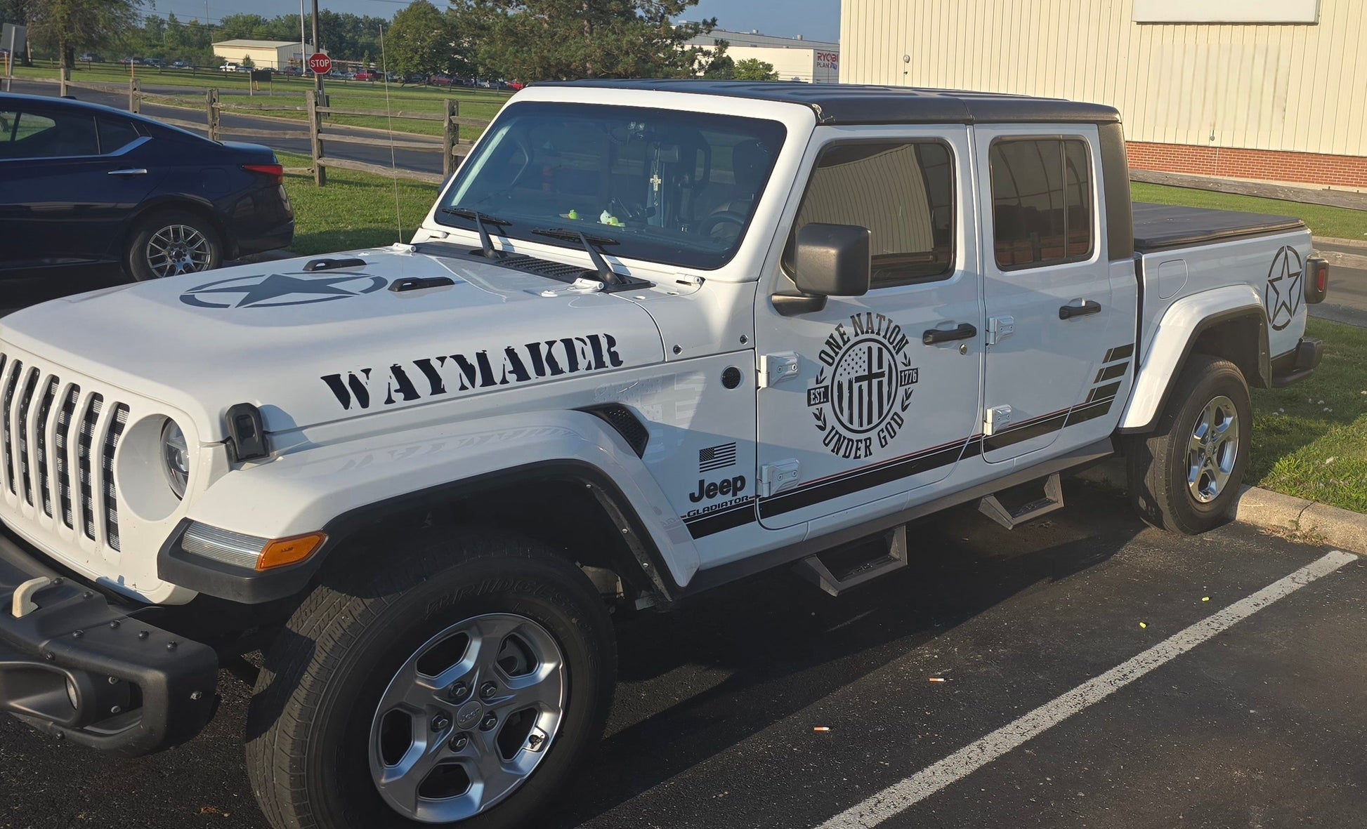 White Jeep truck with 'Waymaker' branding and One Nation Under God graphic on Door parked on a street.