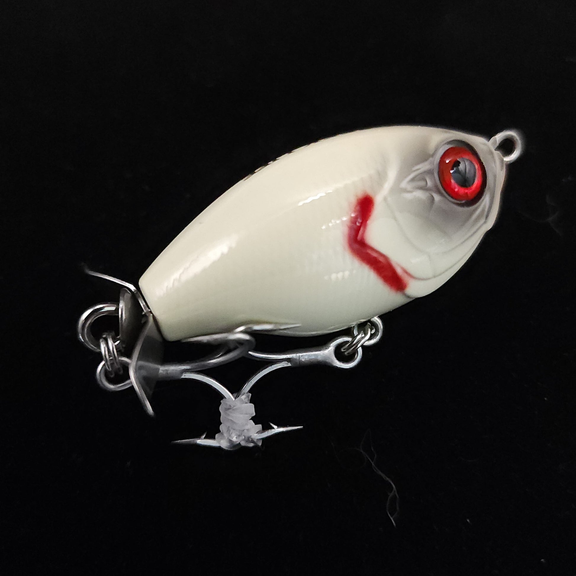 White fishing lure with red eye and chain on a black background
