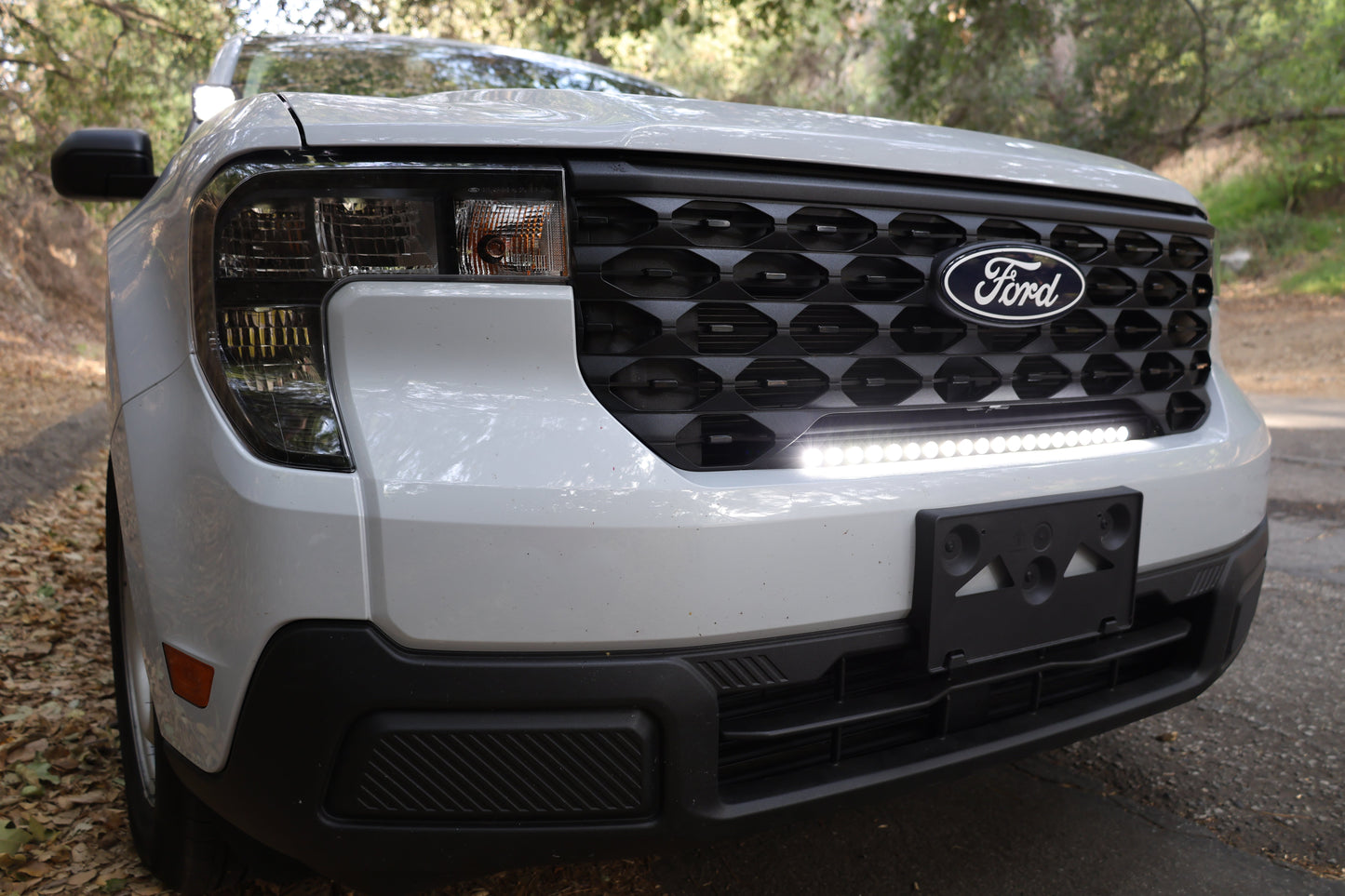 Front view of a white Ford vehicle with a visible grille, headlights and light bar.