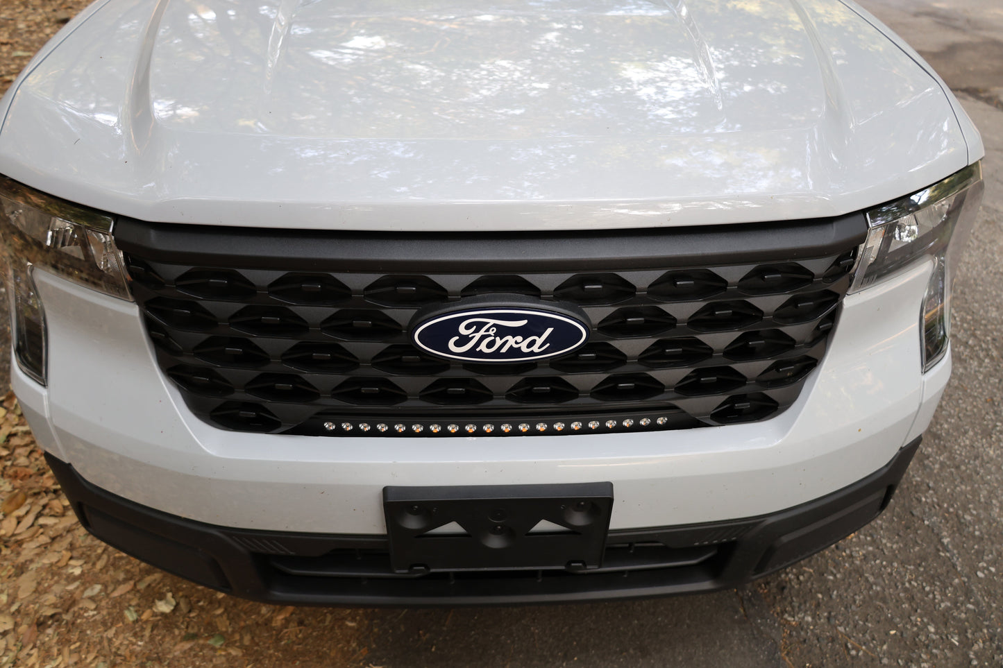 Close-up of a white Ford vehicle's front grille with light bar.