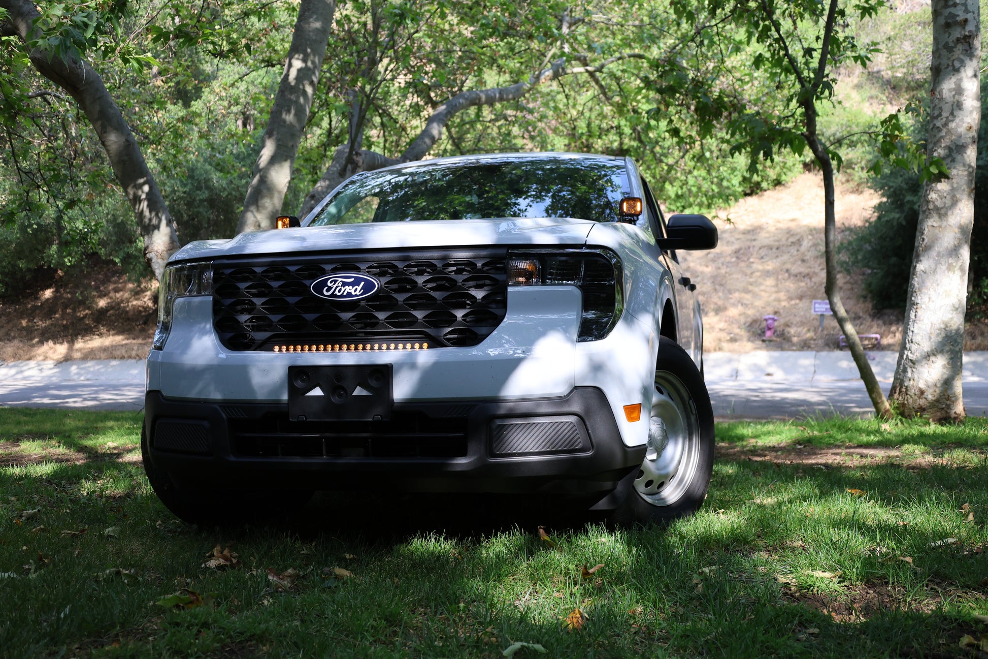Ford vehicle with amber light bar parked on grass with trees in the background