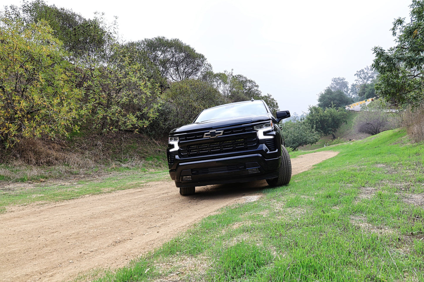 Black Chevrolet truck driving on a dirt road surrounded by trees