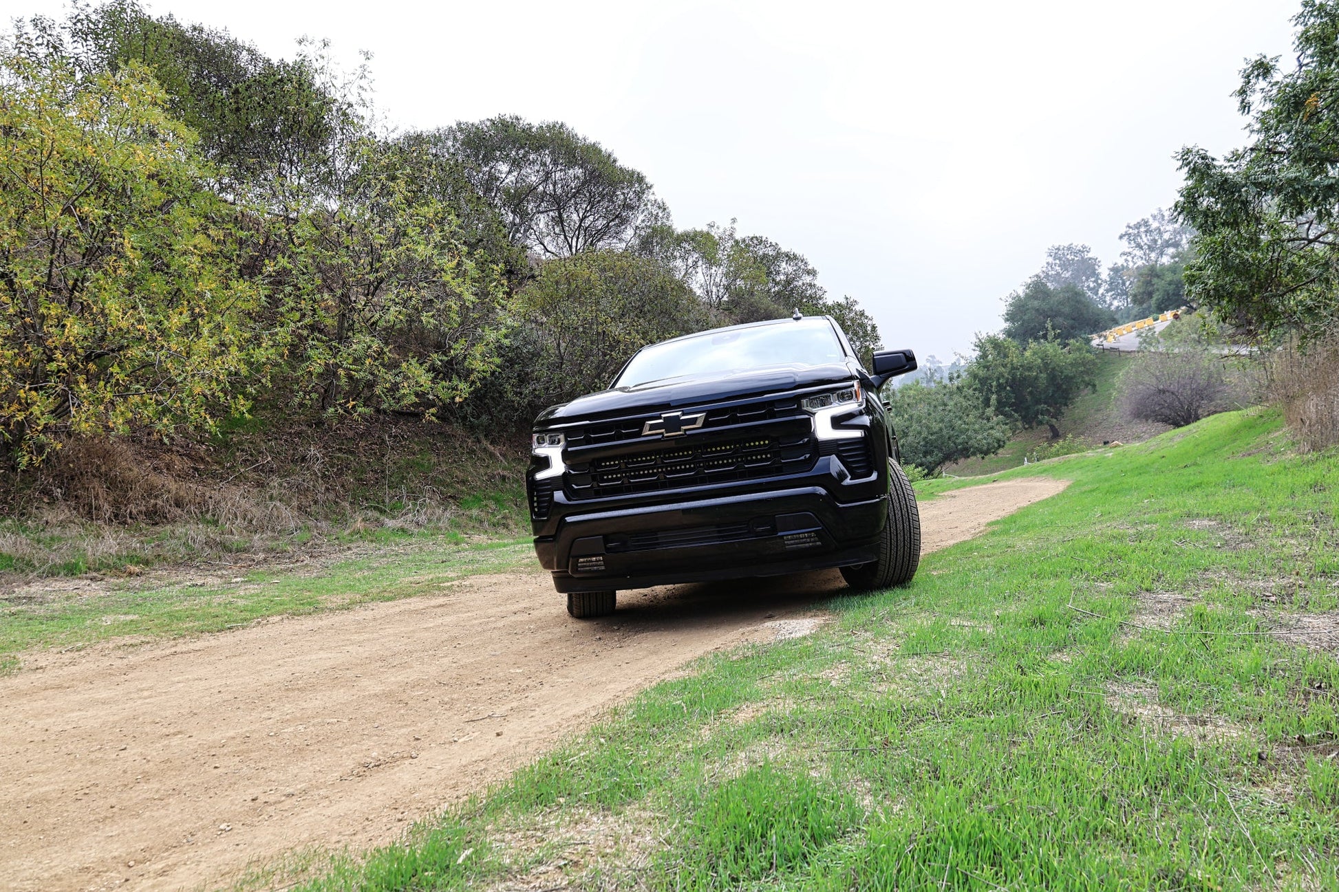 Black Chevrolet truck driving on a dirt road surrounded by trees