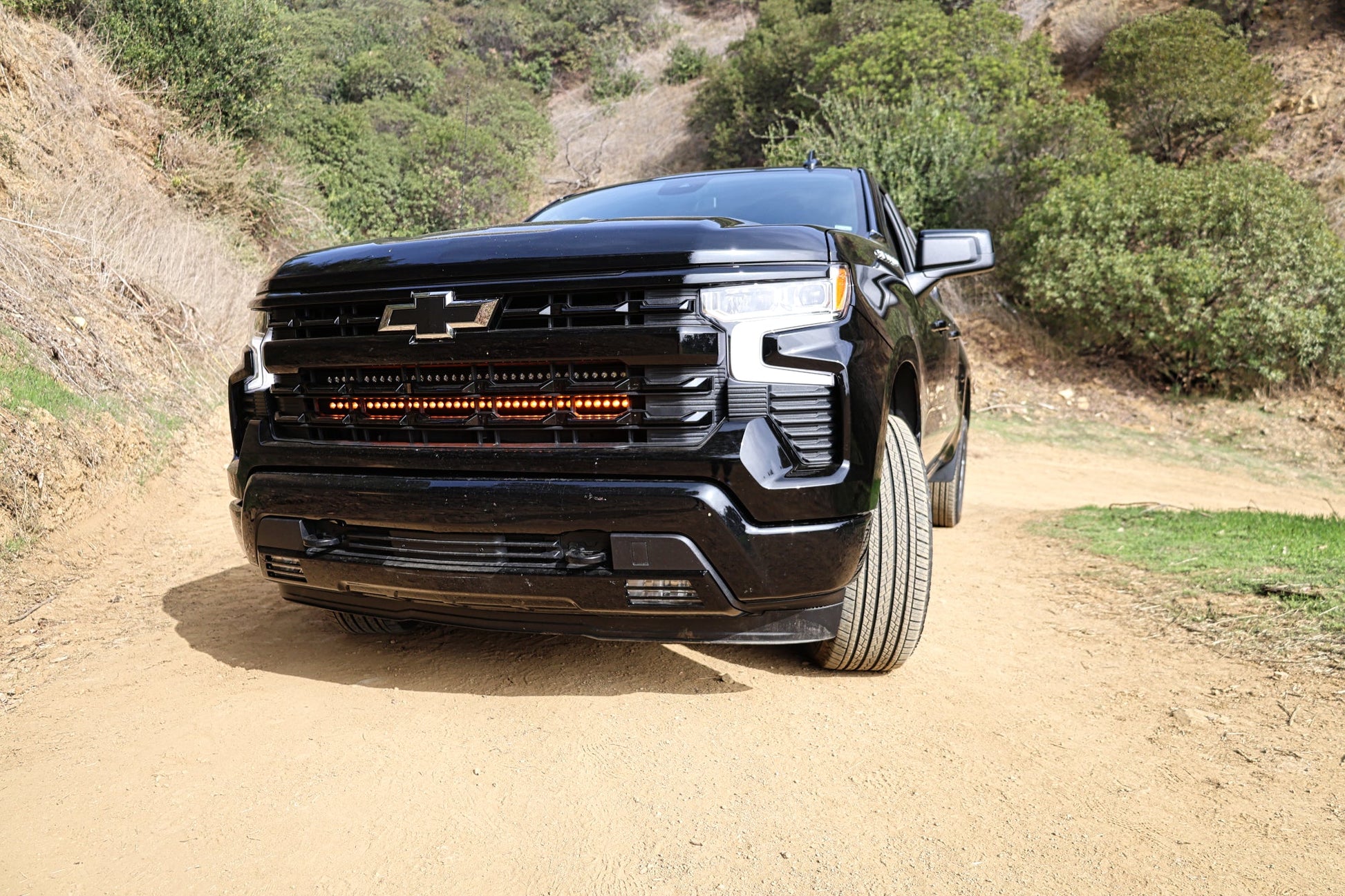 Black Chevrolet truck on a dirt road with greenery in the background and amber LED Light Bar Mounted on front