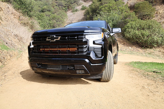Black Chevrolet truck on a dirt road with greenery in the background and amber LED Light Bar Mounted on front
