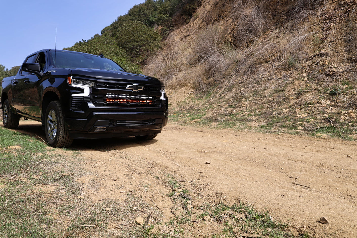 Black Chevrolet truck on a dirt road with a mountainous background and LED Light bars mounted within the Grille