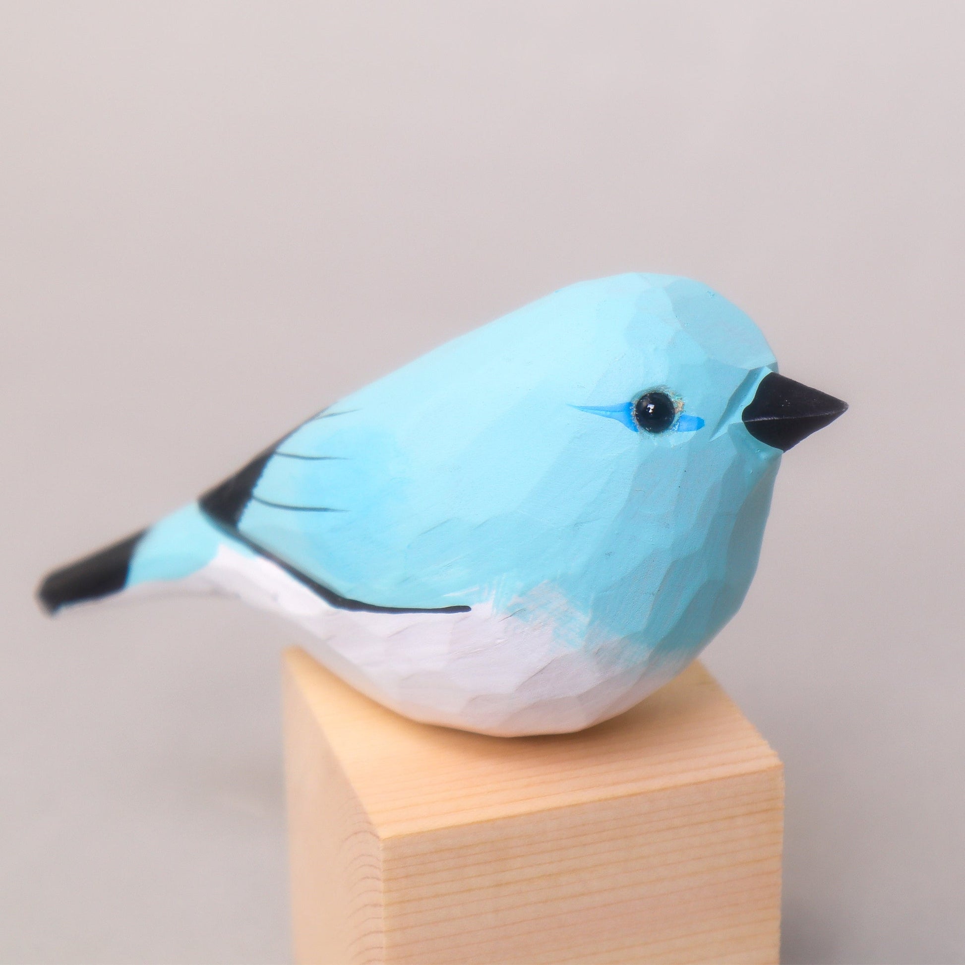 Blue bird figurine on a wooden block against a plain background