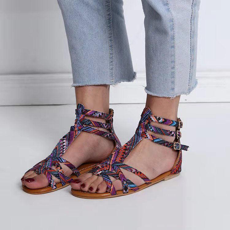 Colorful woven sandals worn with light blue jeans on a white floor.