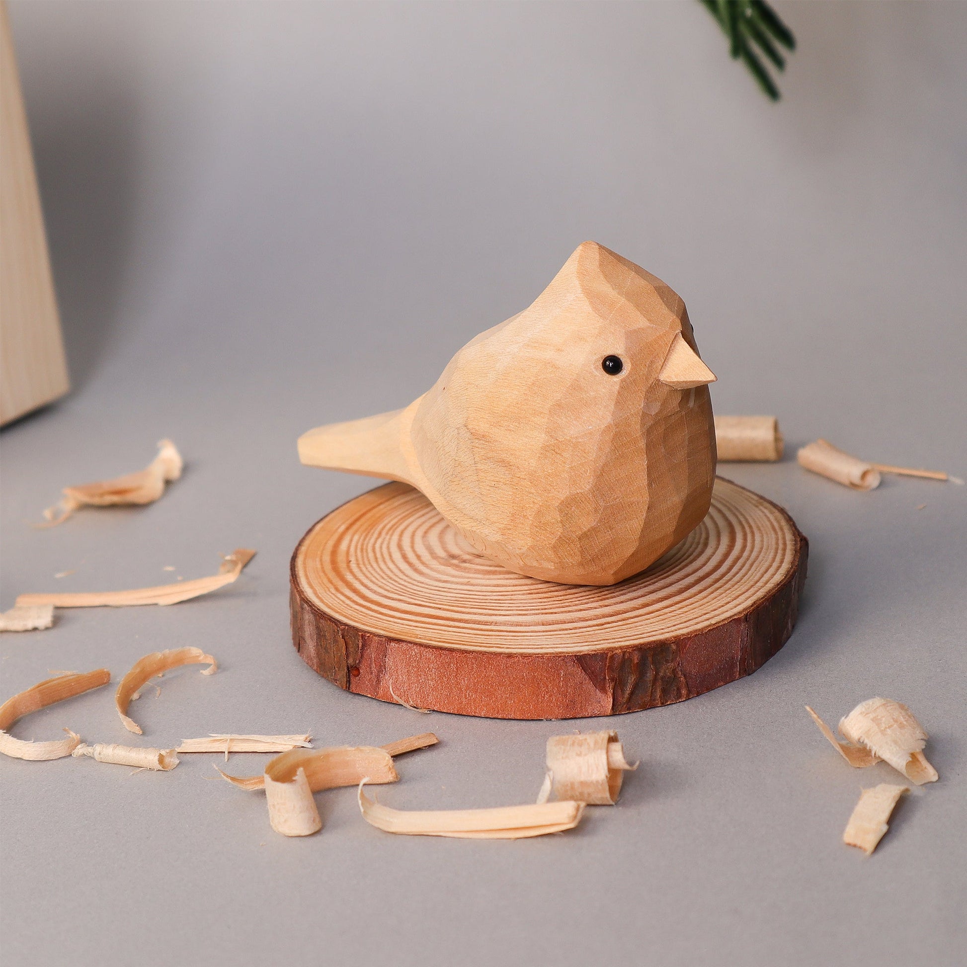 Wooden bird figurine on a wooden base with wood shavings on a gray background