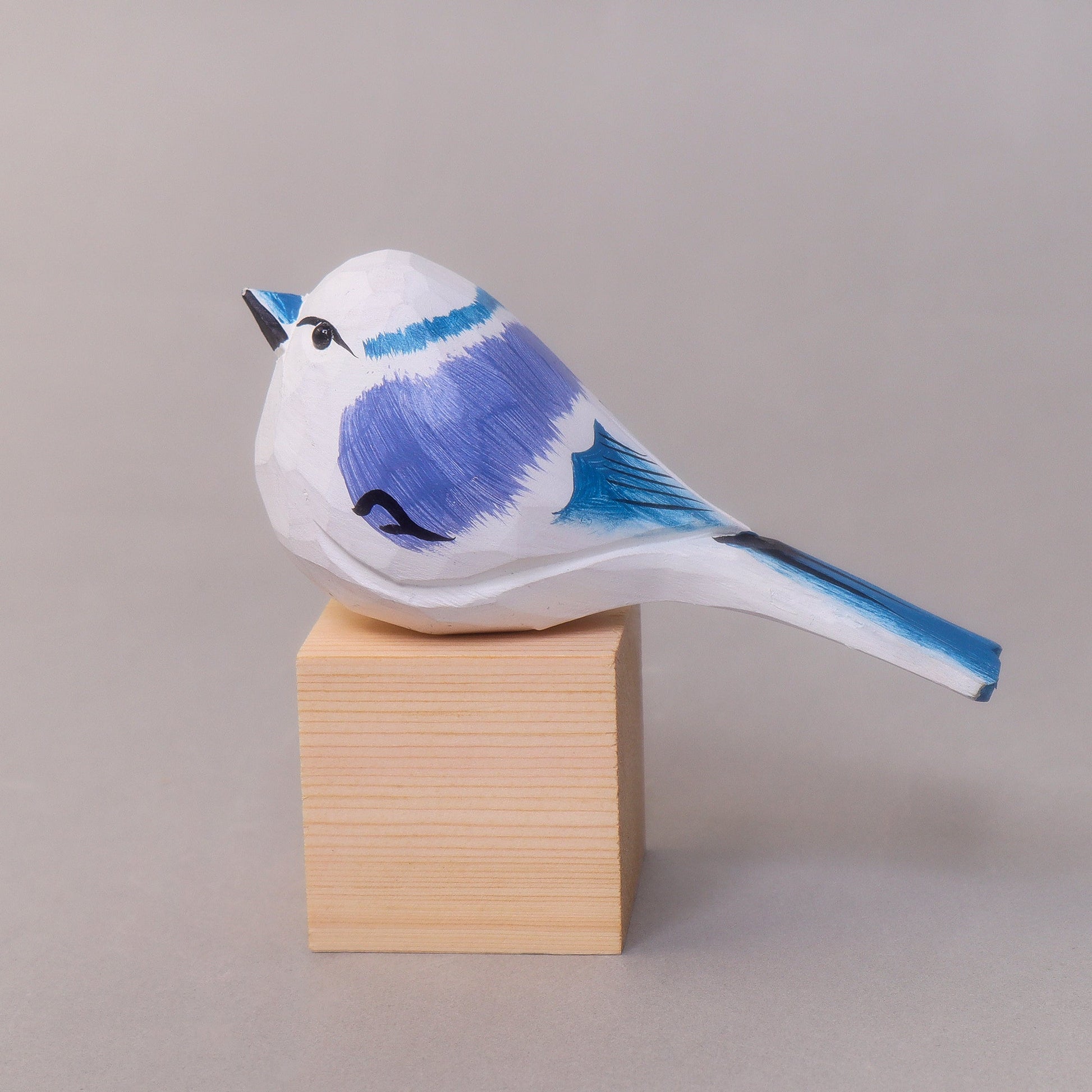 Blue and white wooden bird figurine on a wooden block against a gray background