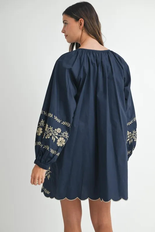 Navy blue dress with floral embroidery on long sleeves worn by a person against a white background
