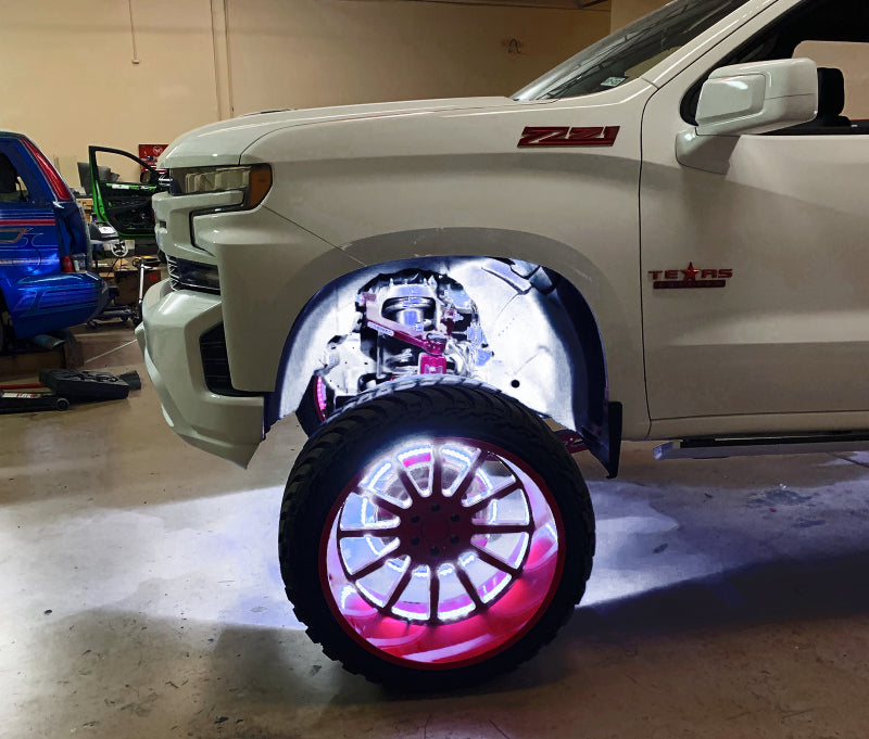 White truck with a custom wheel featuring underbody LED lighting in a garage.