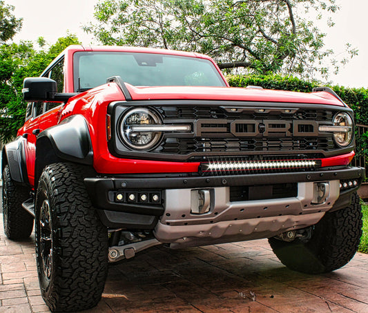 Red pickup truck with large grille and off-road tires on a brick driveway.