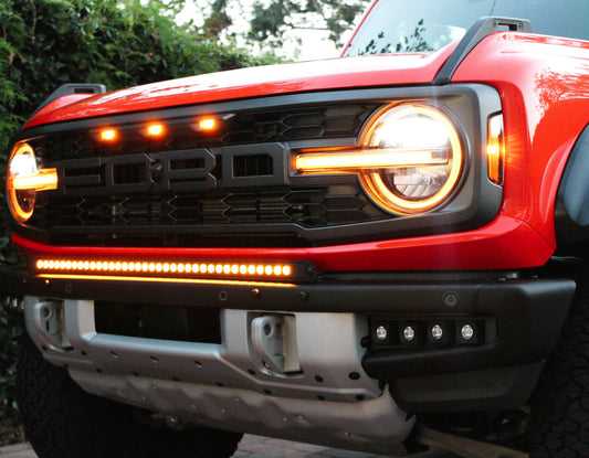 Close-up of a red Ford Bronco's front grille with illuminated headlights.