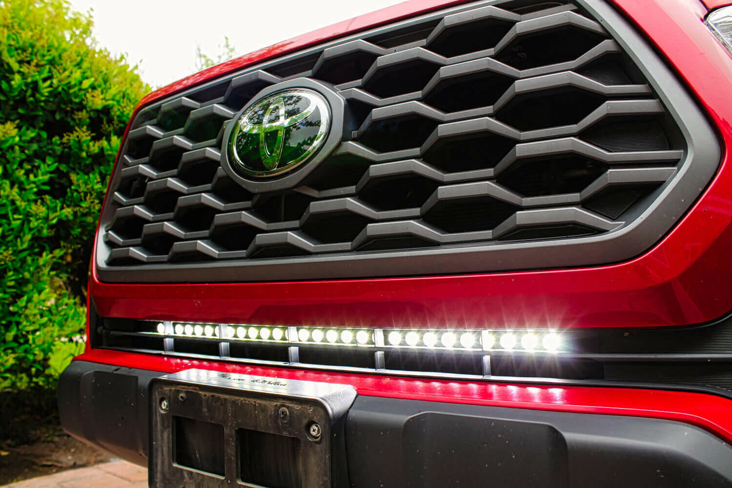 Close-up of a red toyotas grille with a LED Light Bar mounted, set against a blurred green background.