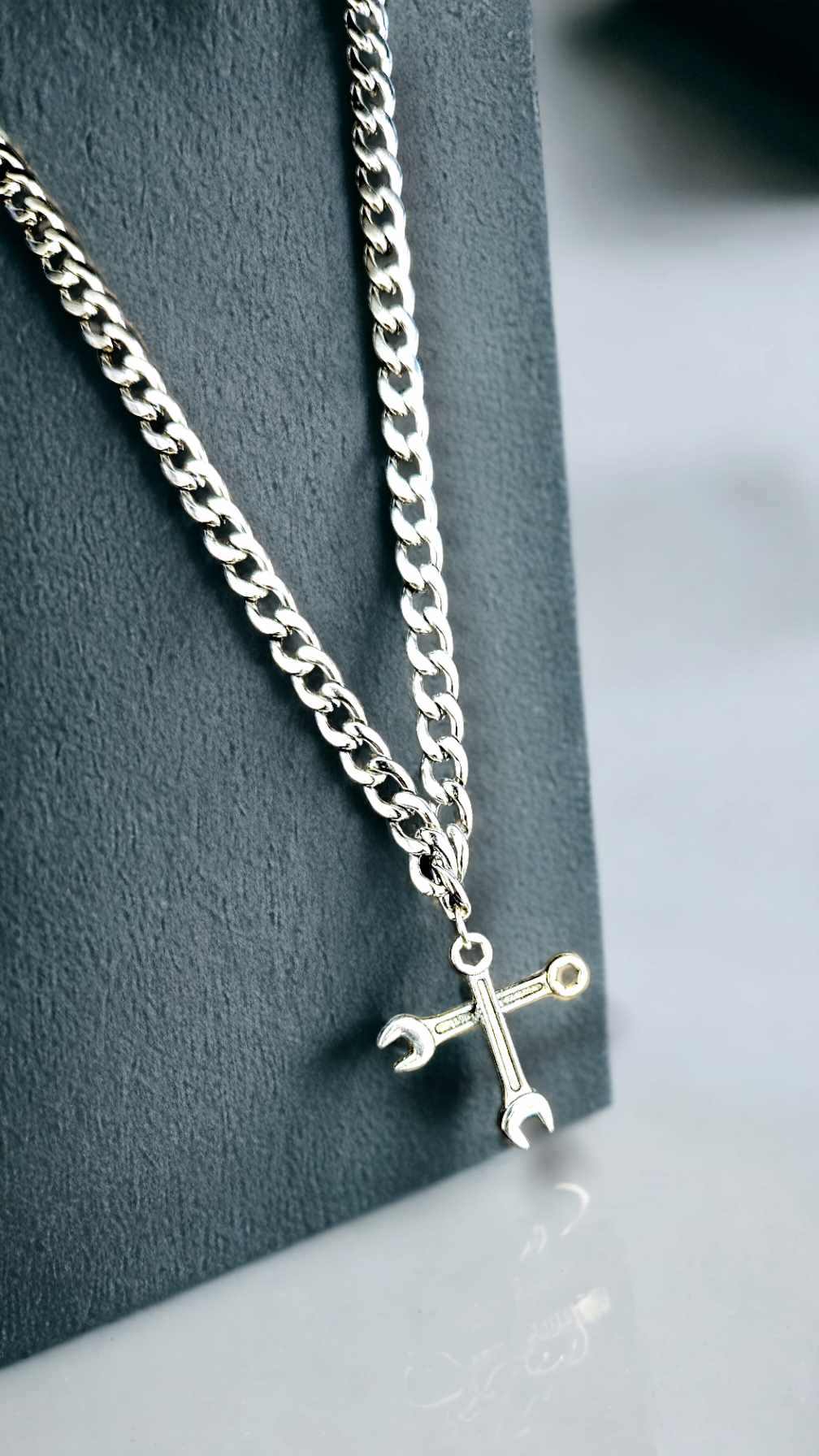 Silver chain necklace with a unique pendant on a dark gray stand.
