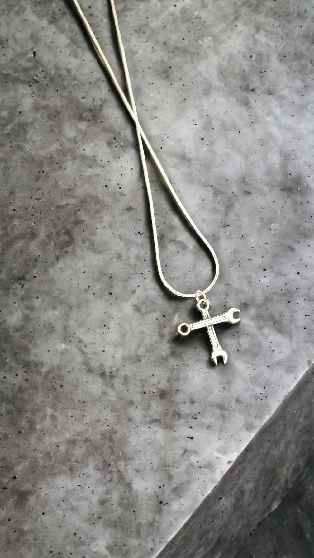 Silver necklace with a cross pendant made of wrenches on a gray concrete surface