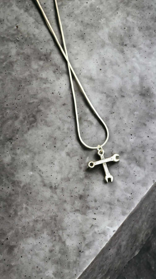 Silver necklace with a cross pendant made of wrenches on a gray concrete surface