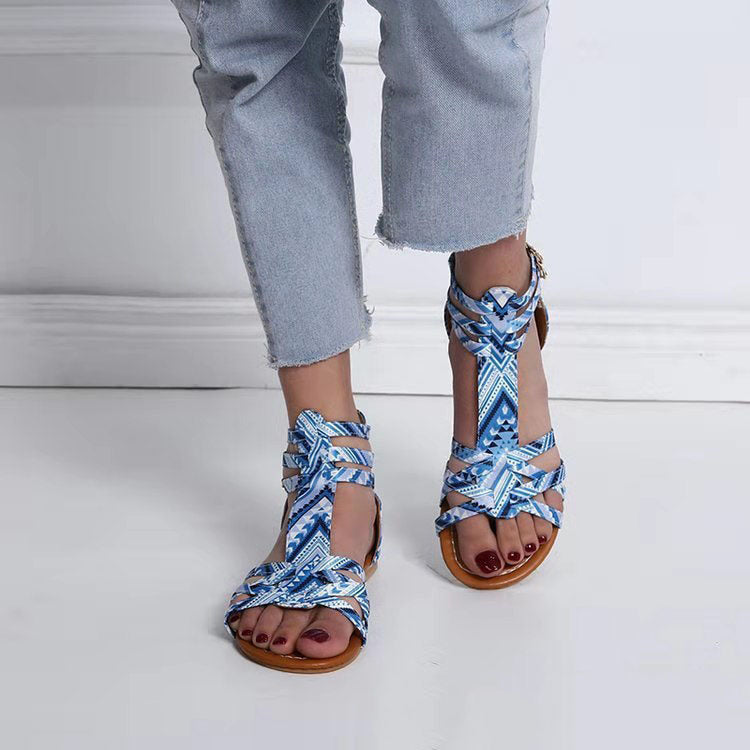 Blue patterned sandals worn with light blue jeans on a white floor.
