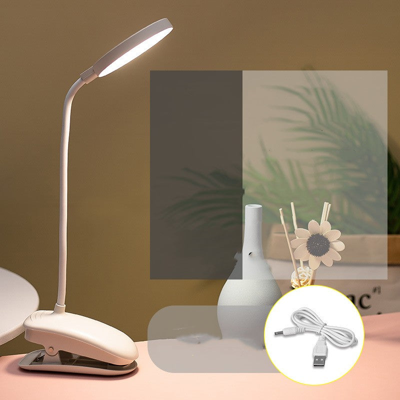 White LED desk lamp with USB cable on a table with decorative items in the background