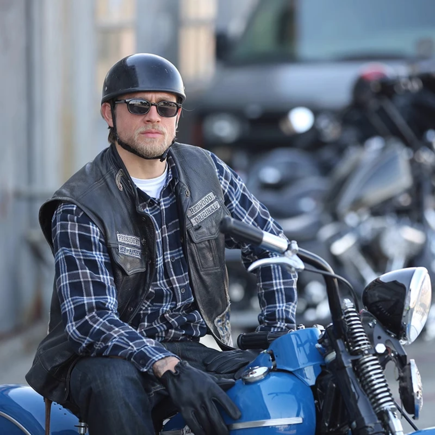 Man sitting on a blue motorcycle wearing a helmet and sunglasses in an urban setting.