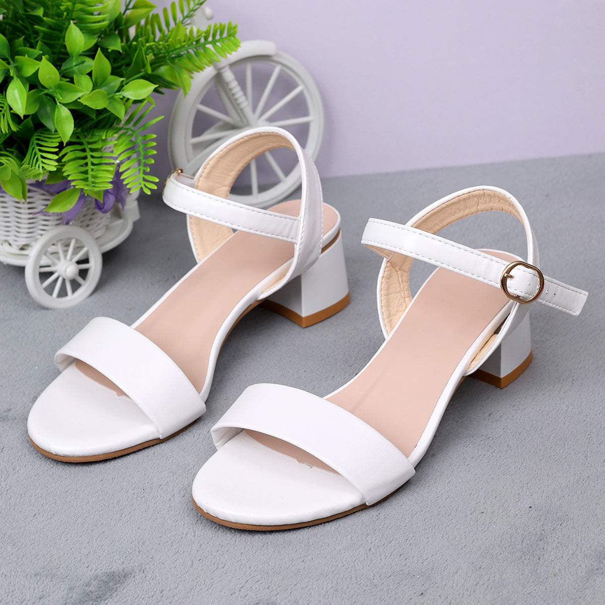 White sandals with a small decorative wheel and plant in the background