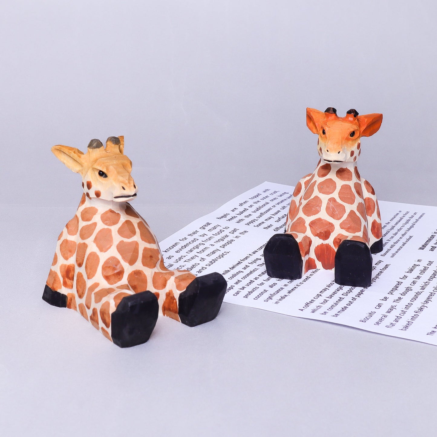 Two toy giraffes on a piece of paper with text on a light gray background