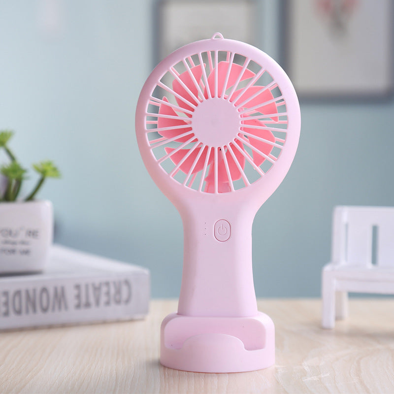Pink handheld fan on a table with a light blue wall and books in the background