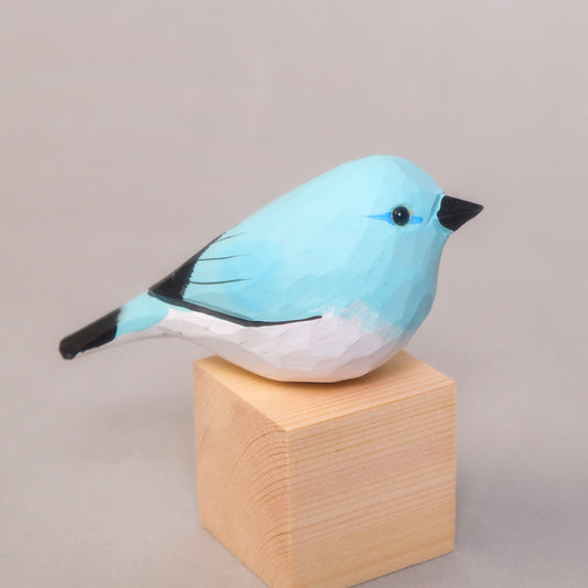Blue bird figurine on a wooden block against a plain background