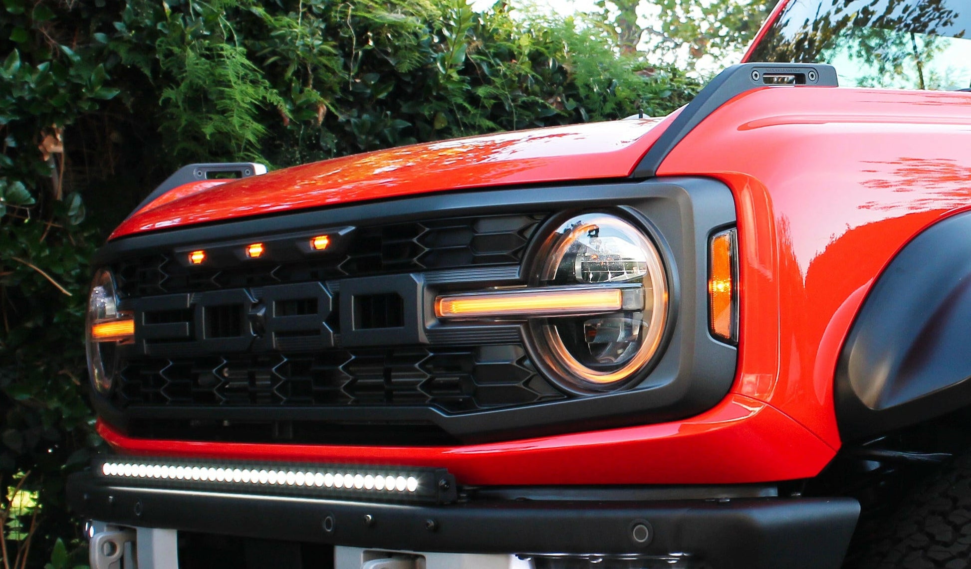 Close-up of a red Ford Bronco with illuminated headlights and grille.
