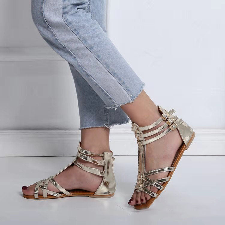 Gold strappy sandals worn with light blue jeans on a white floor.