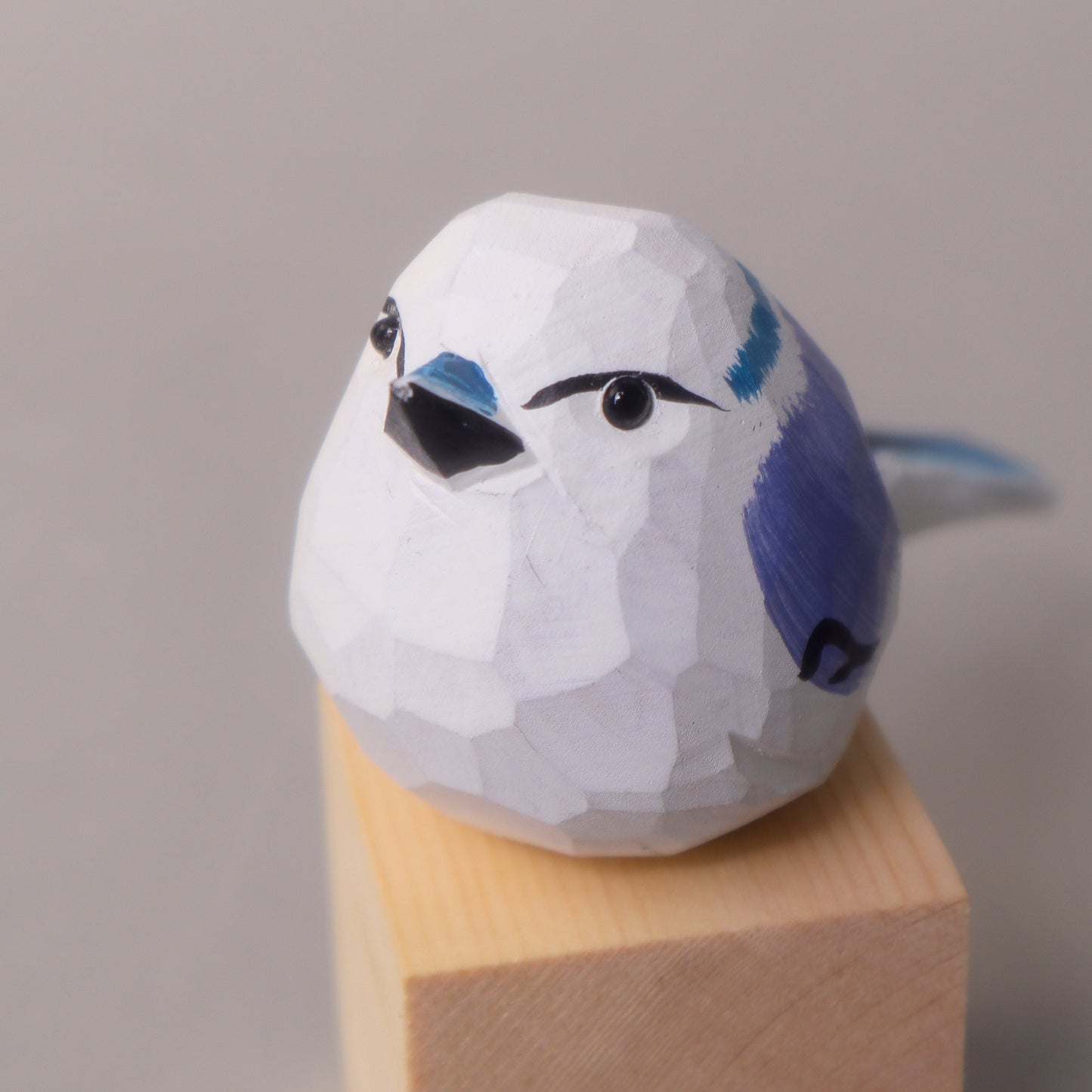 Wooden bird figurine with a white and blue design on a wooden stand against a gray background