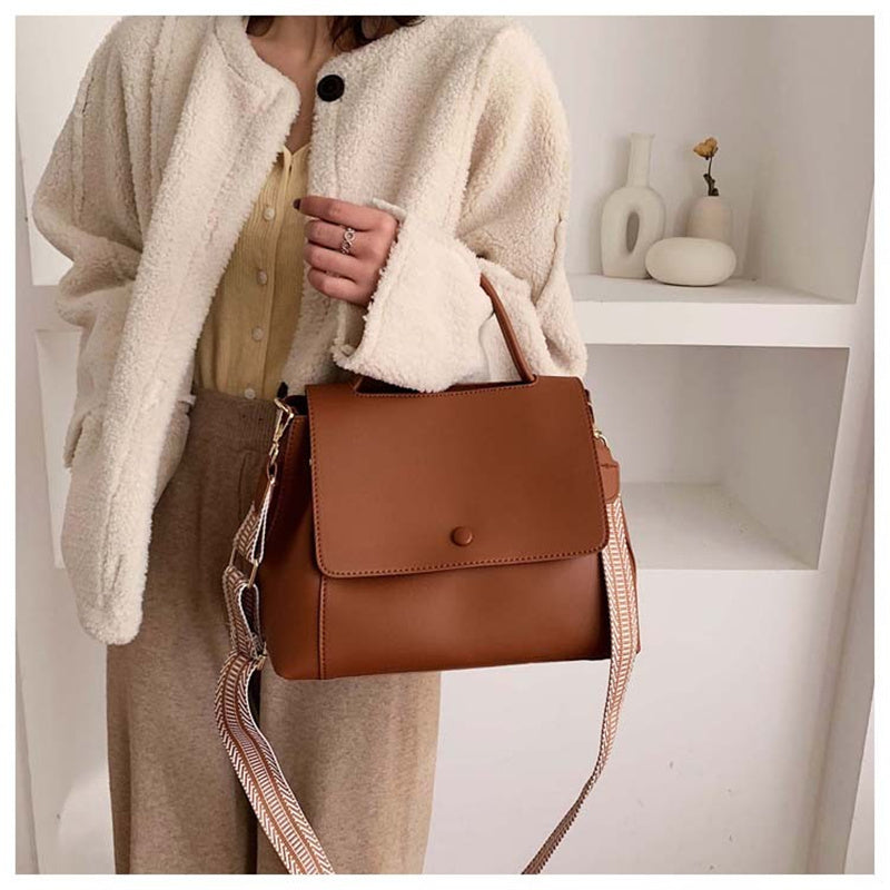 Person holding a brown leather handbag in a minimalistic setting