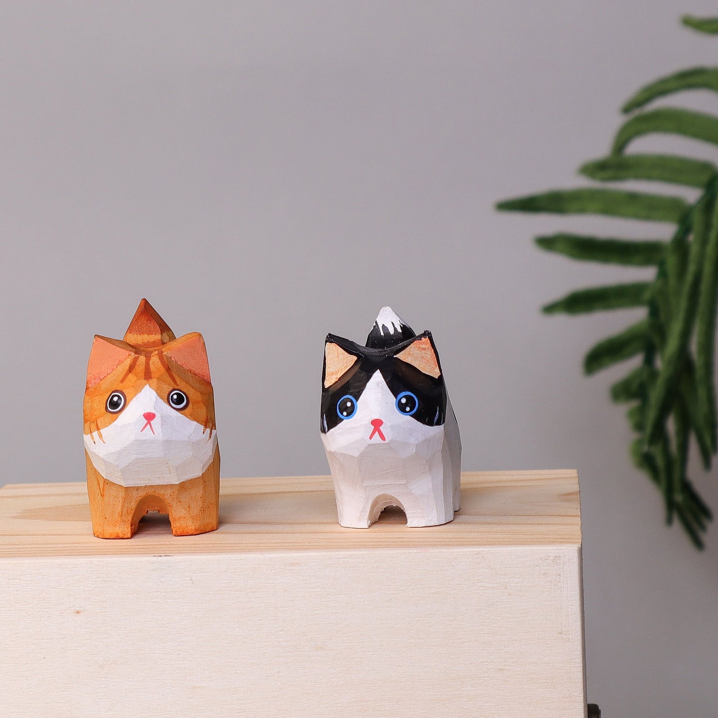 Two Hand-Carved Wooden Cats on a wooden surface with a plant in the background.