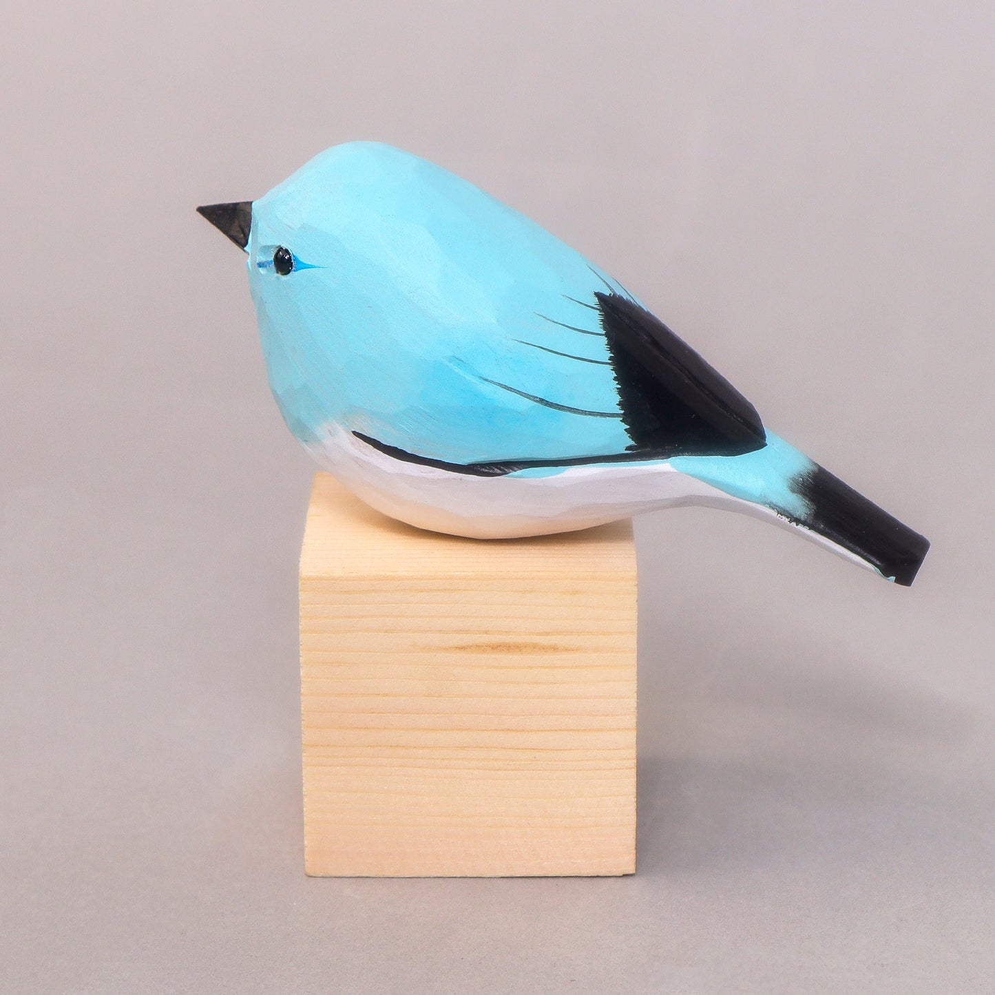 Blue bird figurine on a wooden block against a gray background