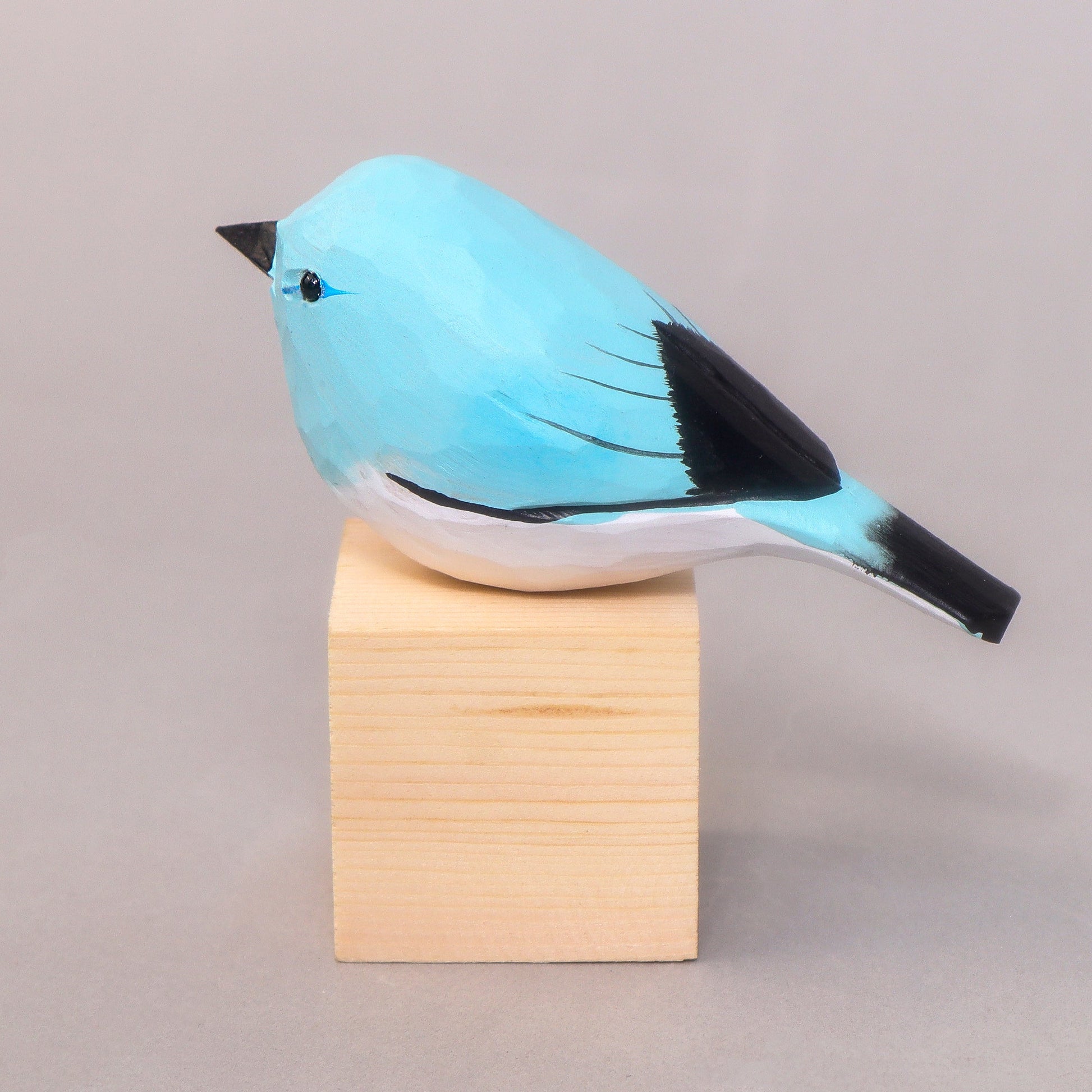 Blue bird figurine on a wooden block against a gray background