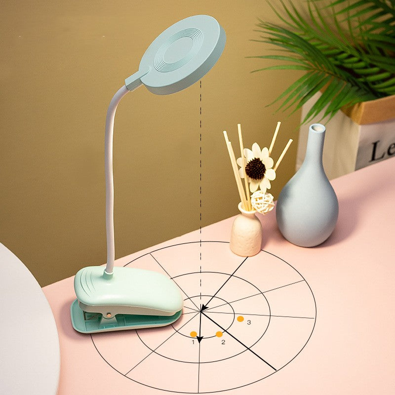 Light blue desk lamp on a pink surface with decorative items and a plant.