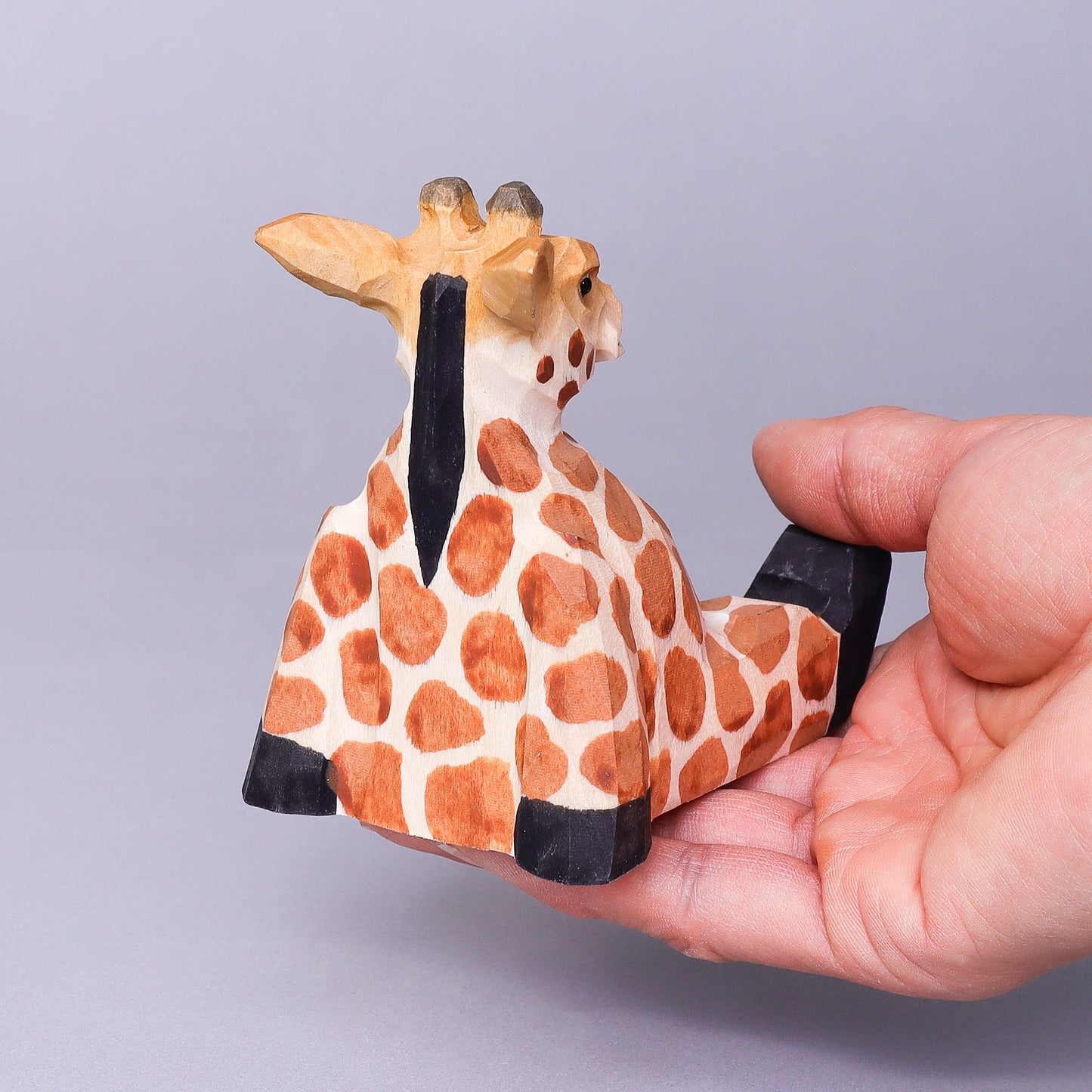 Hand holding a small giraffe figurine against a plain background