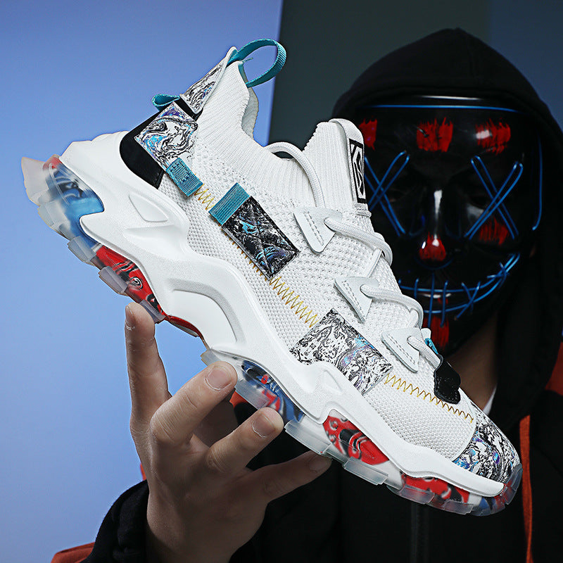 White sneakers with colorful designs held by a person wearing a black hoodie and mask.