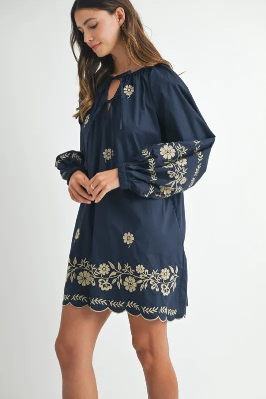 Woman wearing a navy dress with floral embroidery on a white background