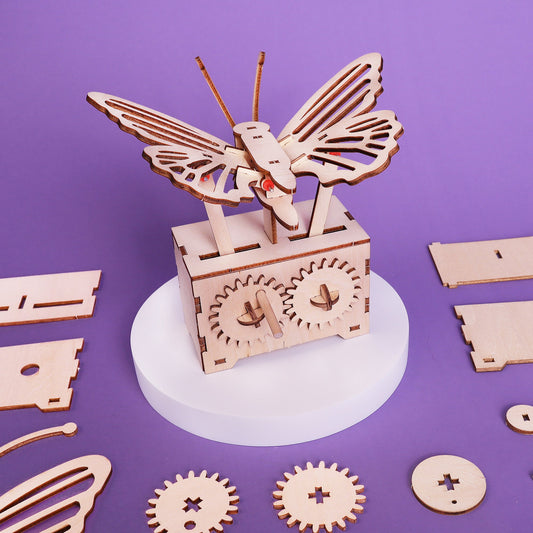 Wooden mechanical butterfly model on a purple background with scattered wooden parts.